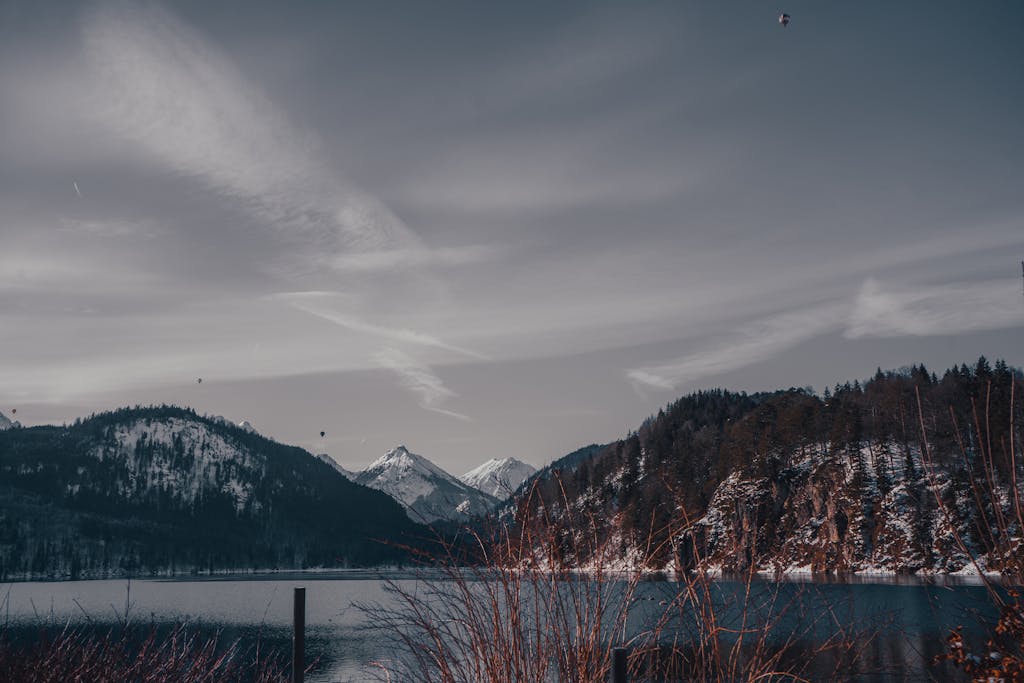A peaceful winter scene featuring snow-capped mountains and a tranquil lake under a cloudy sky.