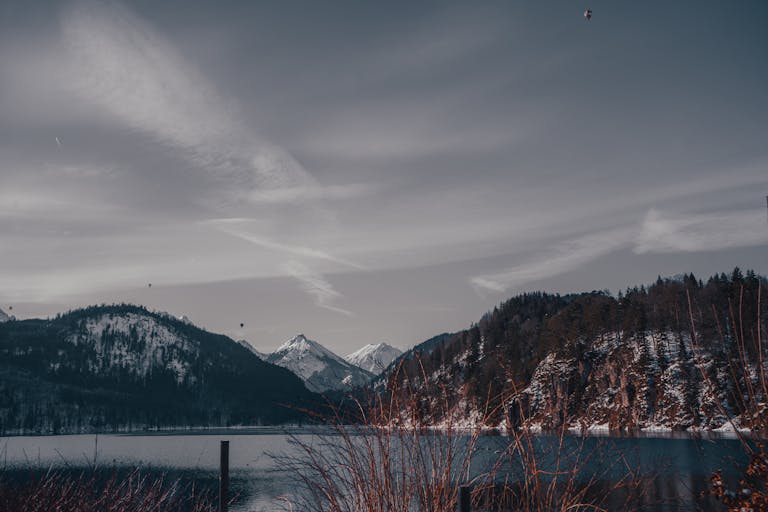 A peaceful winter scene featuring snow-capped mountains and a tranquil lake under a cloudy sky.