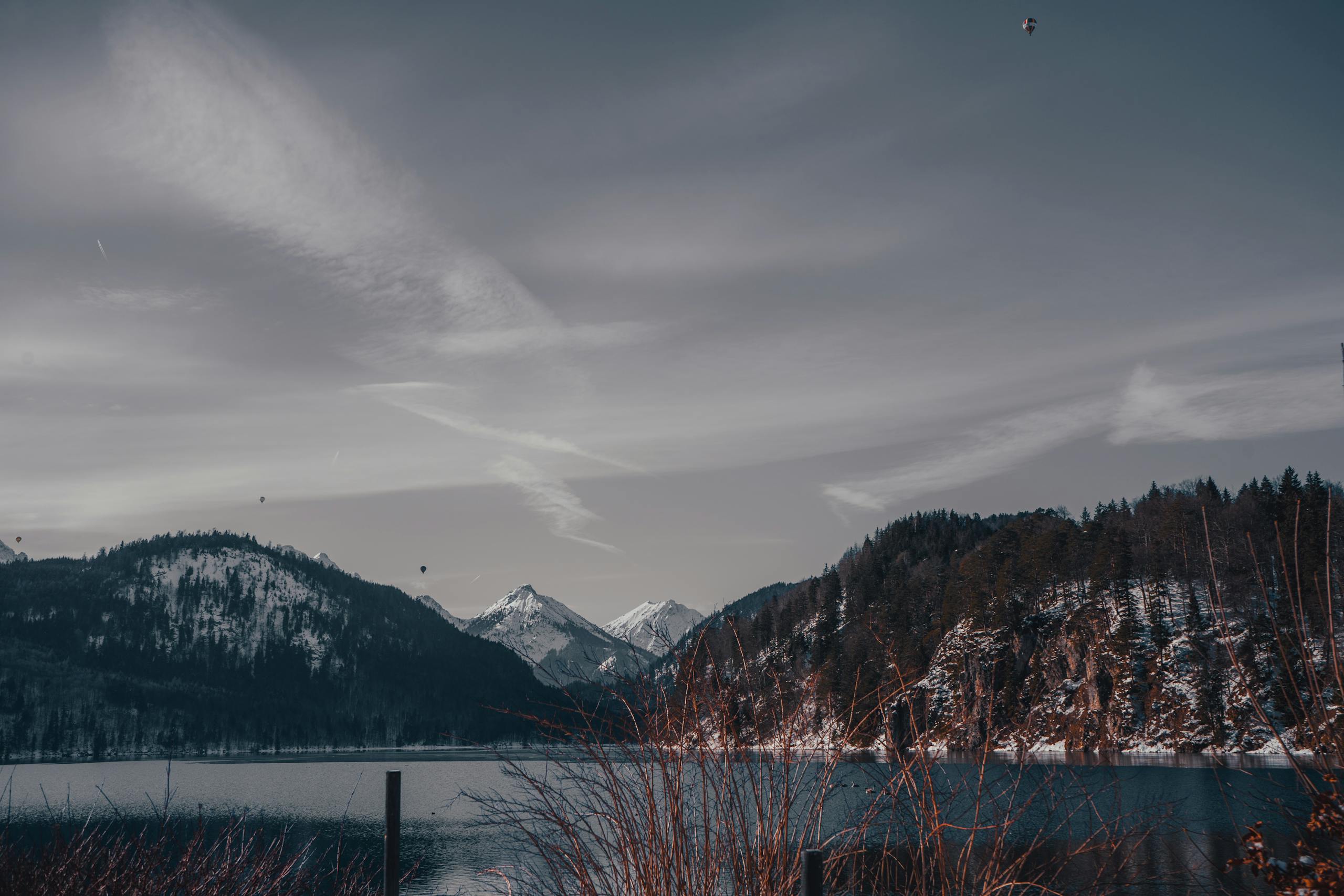 A peaceful winter scene featuring snow-capped mountains and a tranquil lake under a cloudy sky.