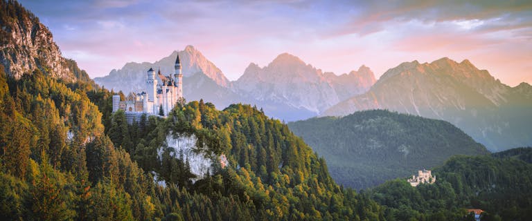 Breathtaking view of Neuschwanstein Castle with Alps in the background during sunset.