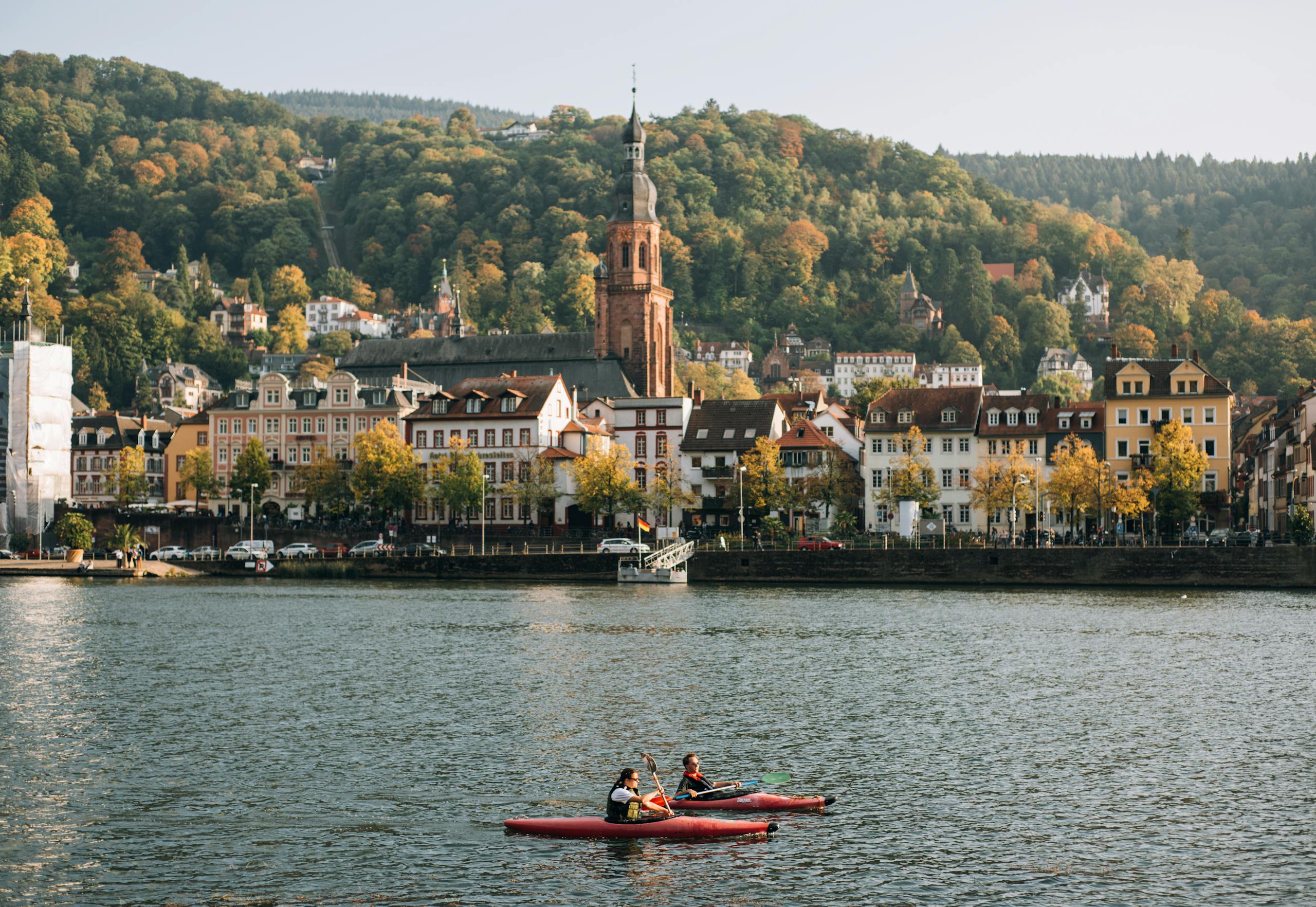 Kayakers on the Neckar River with Heidelberg's charming architecture and lush hills in the background.