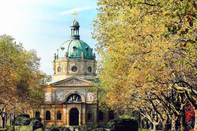 Beautiful cathedral with a green dome surrounded by lush autumn trees in a serene setting.