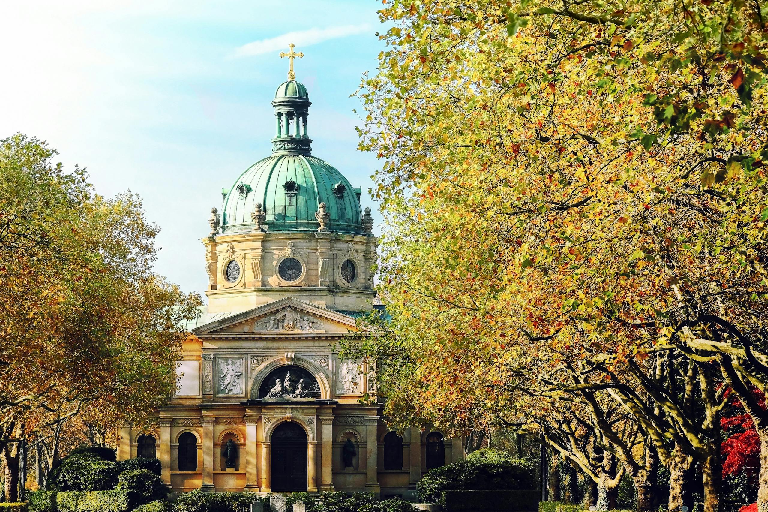 Beautiful cathedral with a green dome surrounded by lush autumn trees in a serene setting.